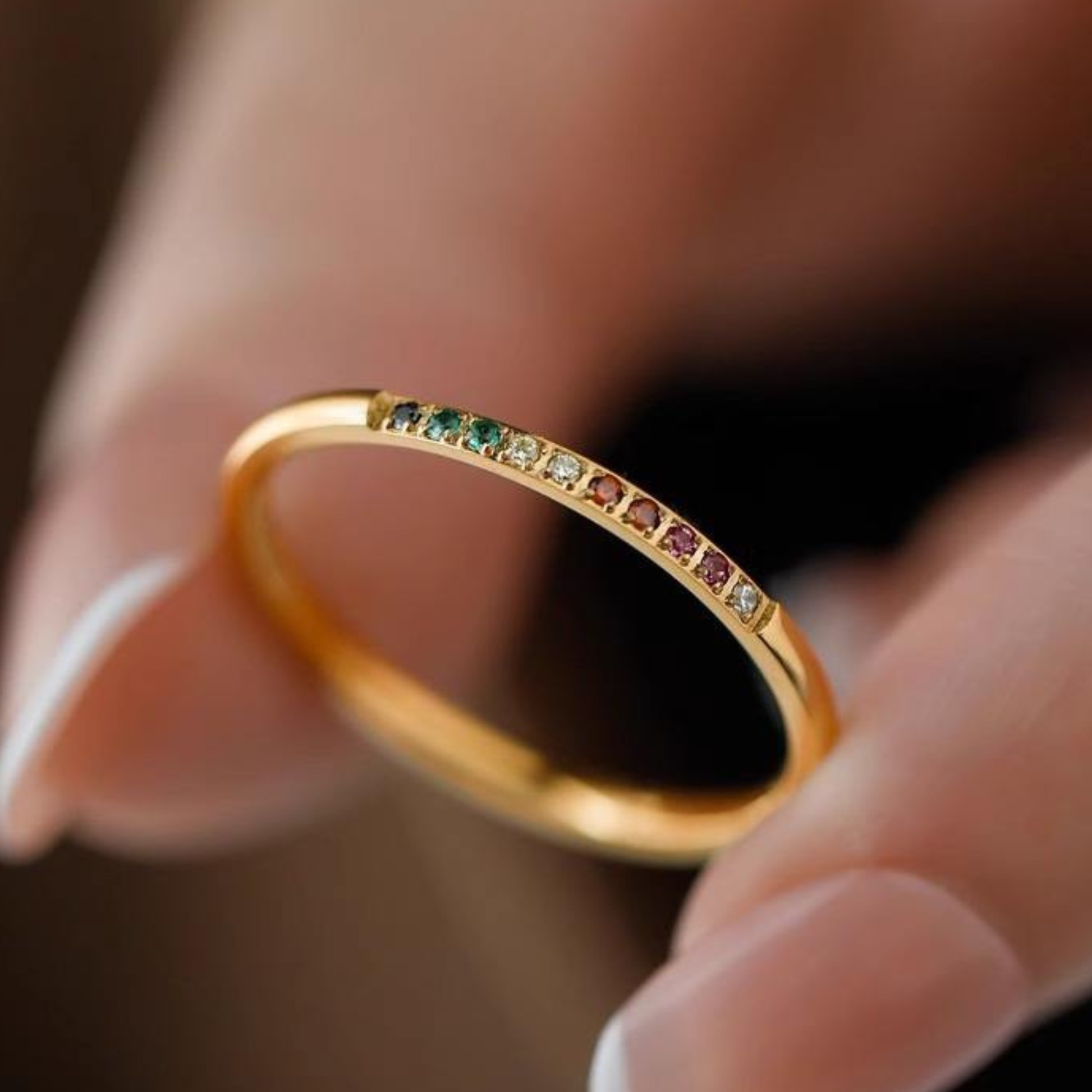 Pretty 18K Gold Plated Stainless Steel Rainbow Band Ring with embedded gemstones held between fingers.
