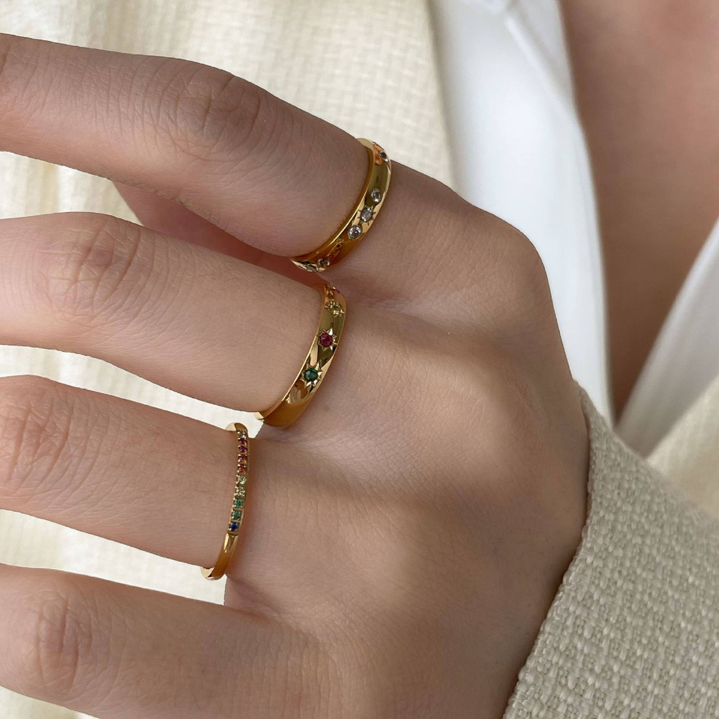 Close-up of a hand wearing a Stainless Steel 18K Gold Plated Celestial Stone Ring and a Stainless Steel 18K Gold Plated Rainbow band Stone Ring neutral background.