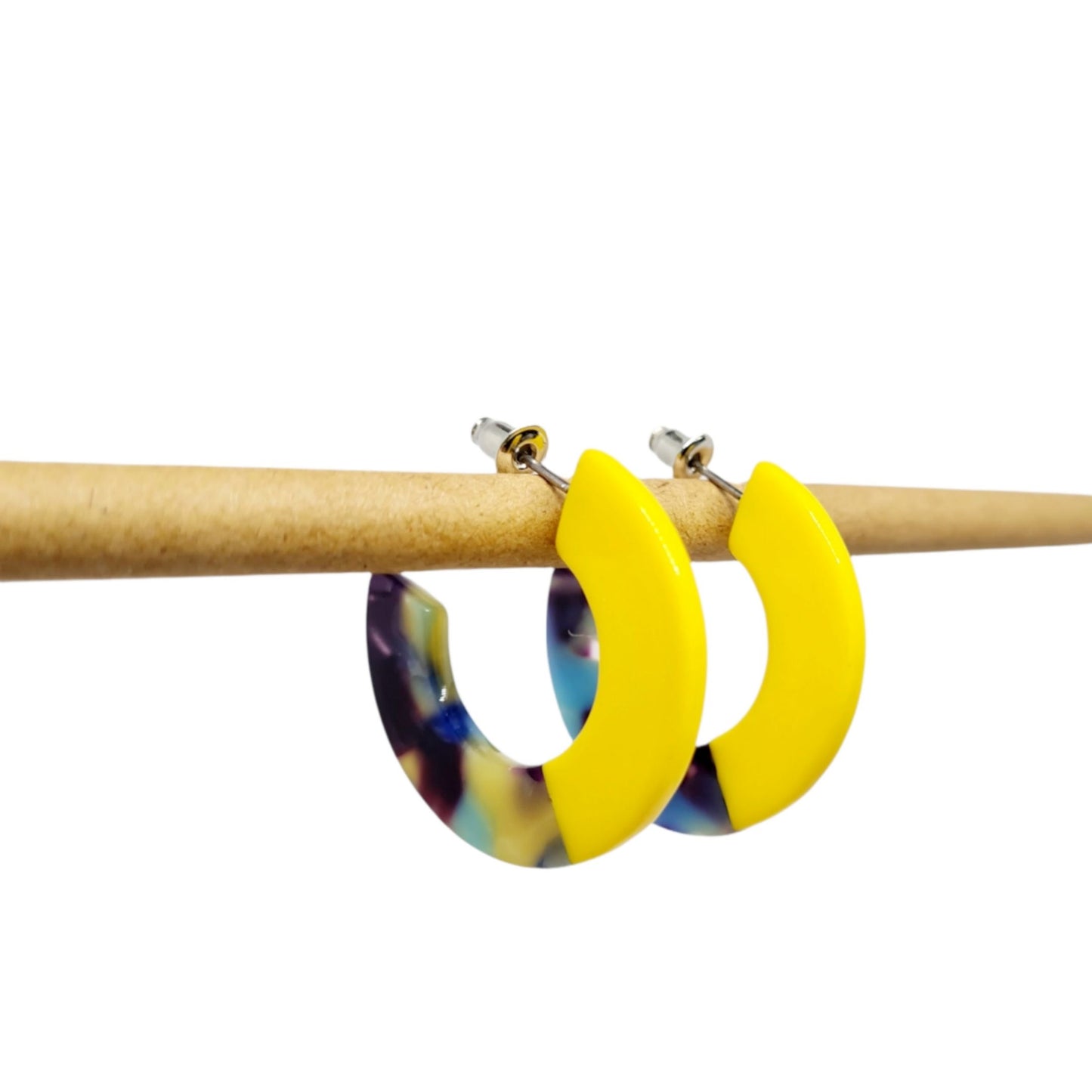 A pair of chunky two-tone mini resin hoop earrings, with one half yellow and the other half multi-colored, on a white surface.
