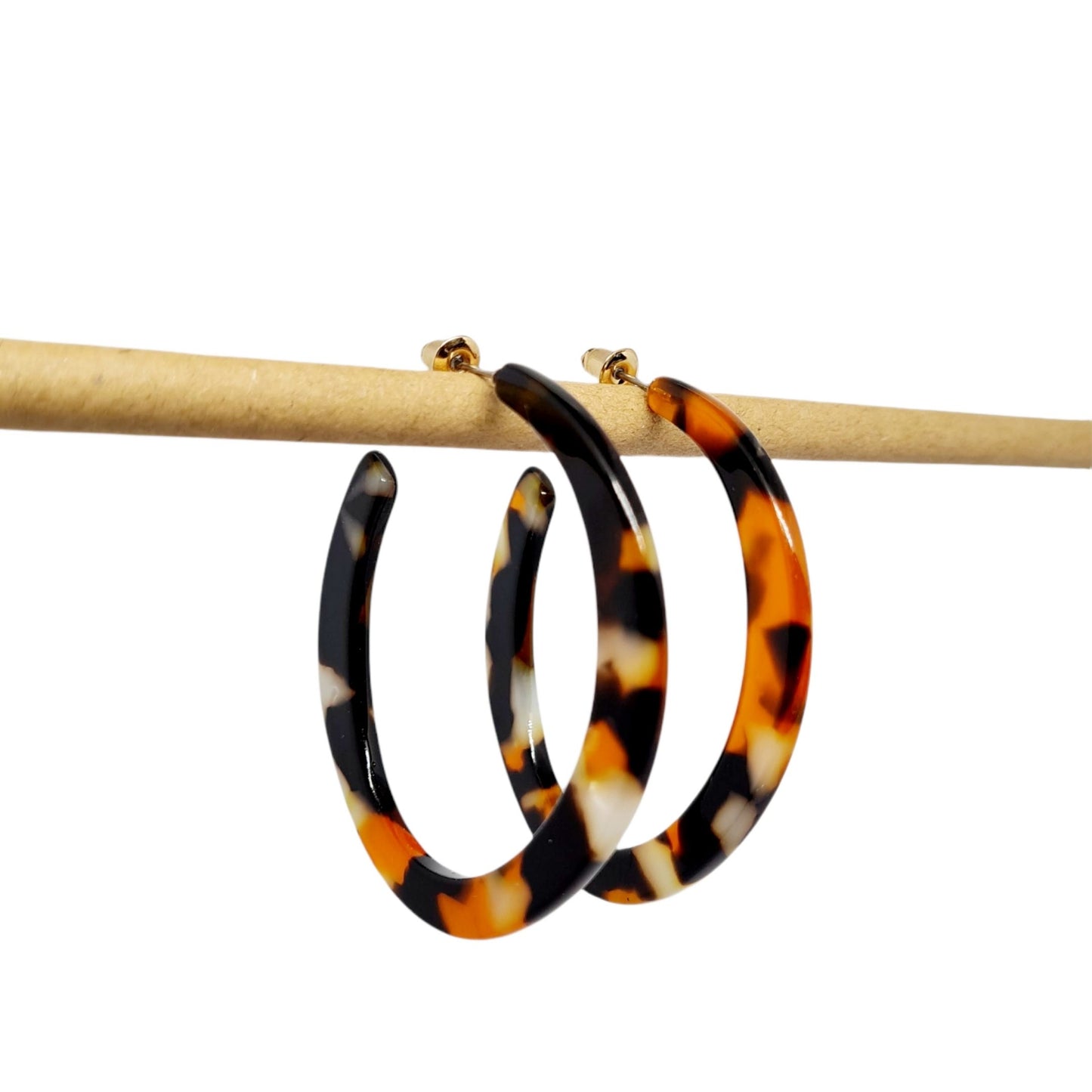 A pair of upcycled flame resin hoop earrings with a gold plated finish, featuring a bold pattern in shades of orange and brown on a white background.