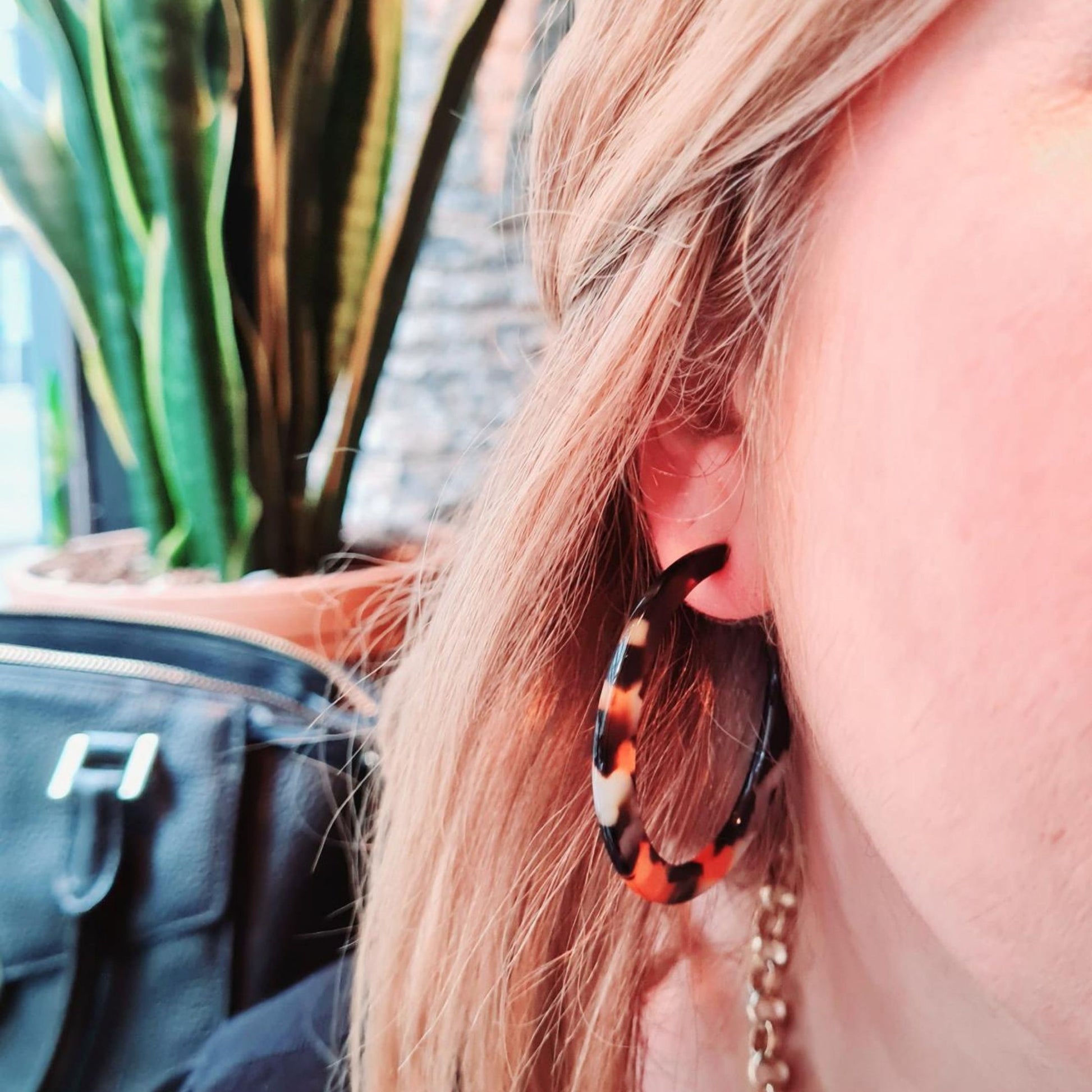 A pair of upcycled flame resin hoop earrings with a gold plated finish, featuring a bold pattern in shades of orange and brown on a girl in the sunlight.