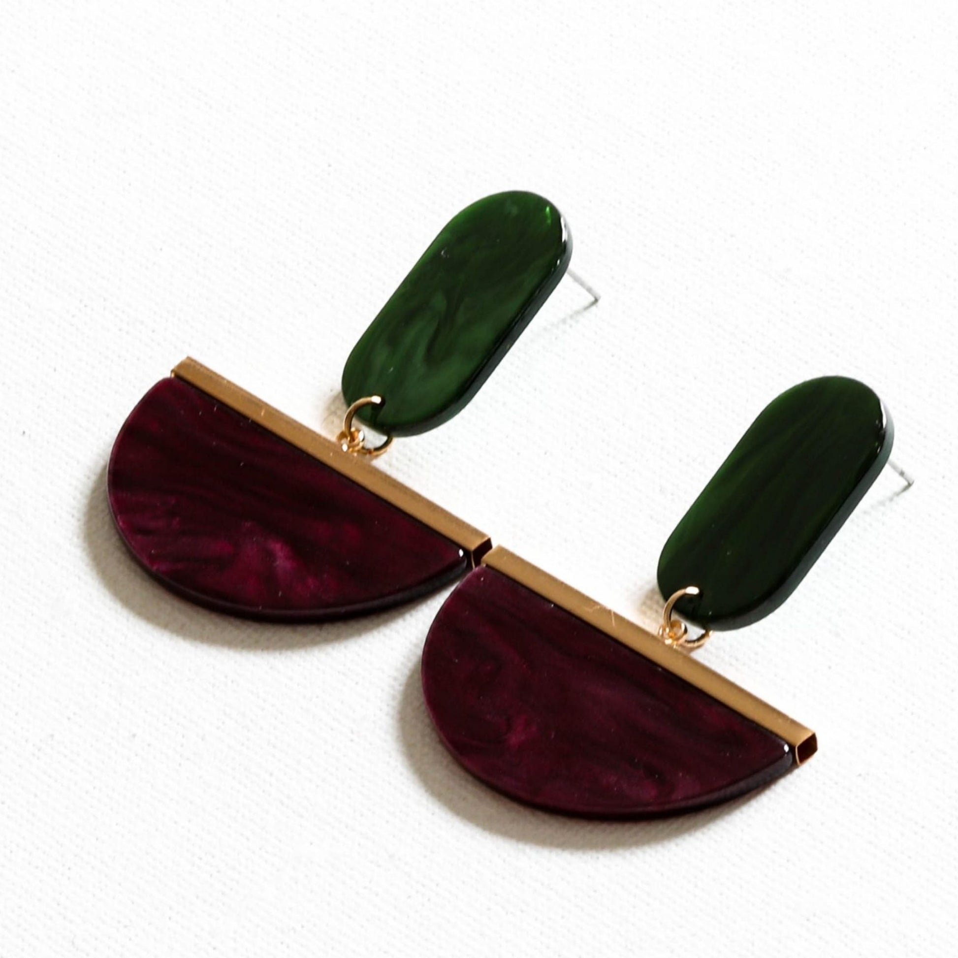 A pair of drop earrings featuring burgundy and green upcycled resin in a geometric design with gold plating on a white background.