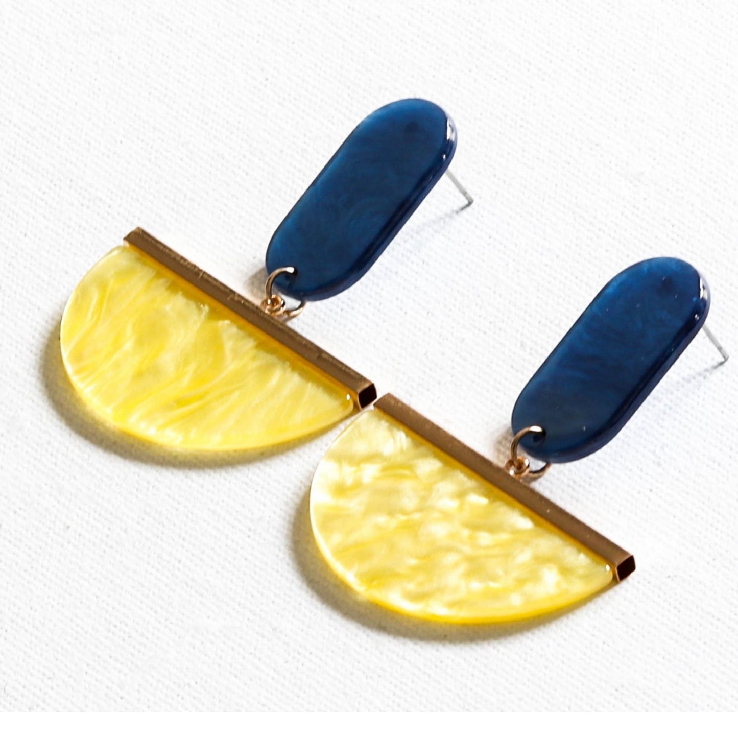 A pair of drop earrings featuring blue and yellow upcycled resin in a geometric design with gold plating on a white background.