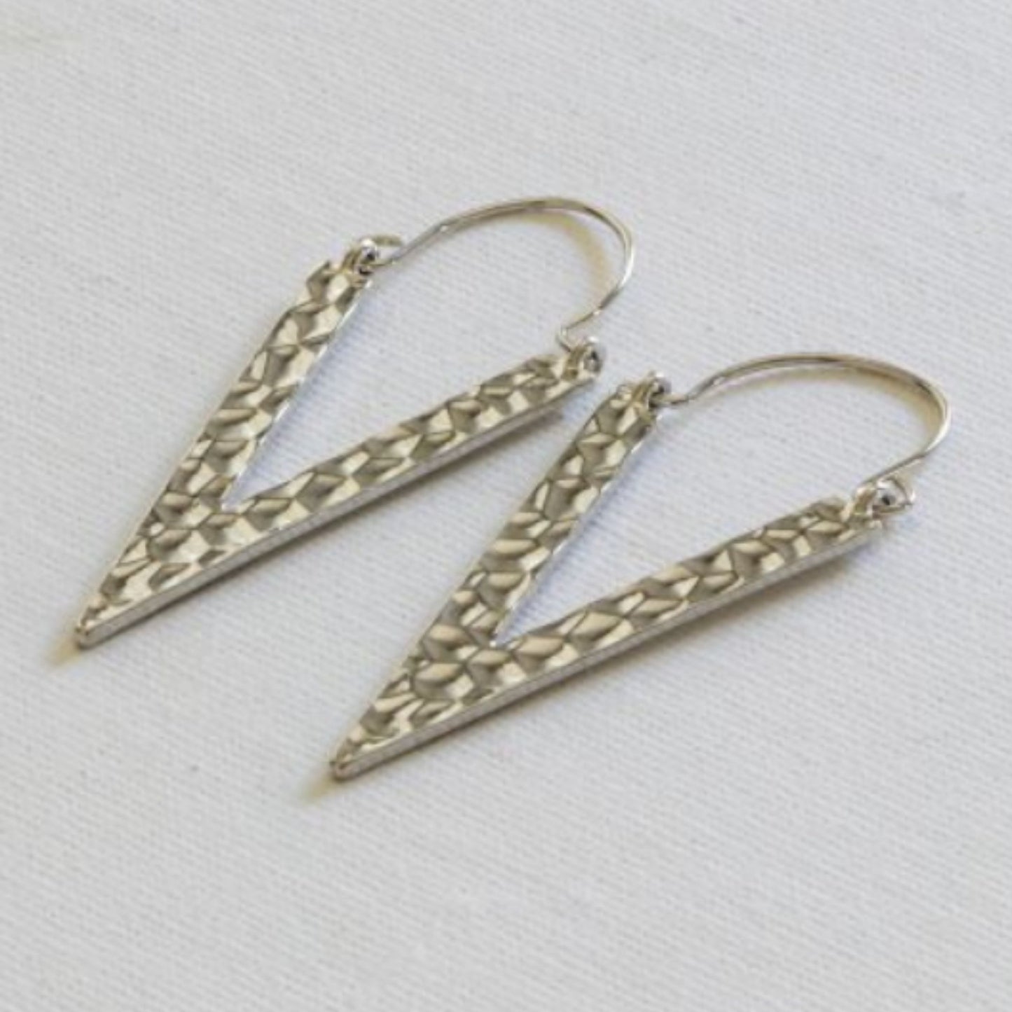 A pair of silver-plated, textured triangle earrings laid on a white surface.