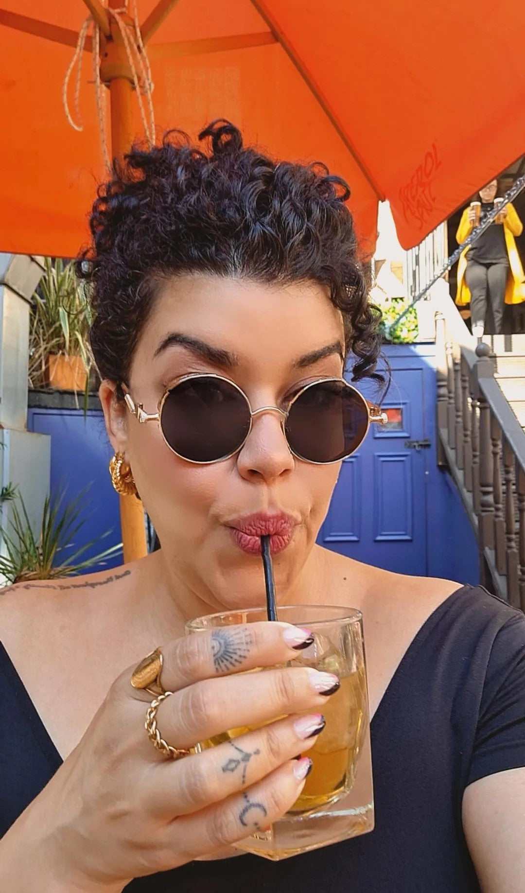 A pair of scallop hooped earrings with 18K gold plating, displayed on a pretty girl with curly hair drinking a cocktail