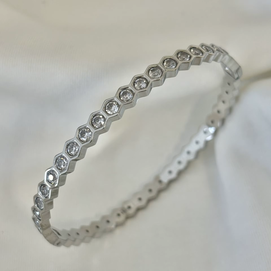 18K Gold plated bangle with glass crystal stones on a soft white fabric background.