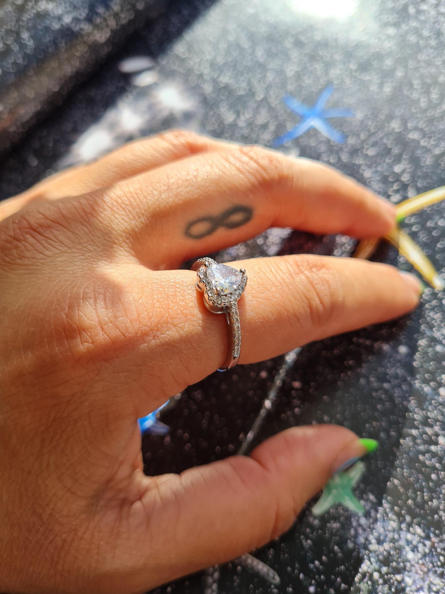 A person's hand displaying an 18k white gold plated sparkle heart ring with a glass cubic zirconia main stone.