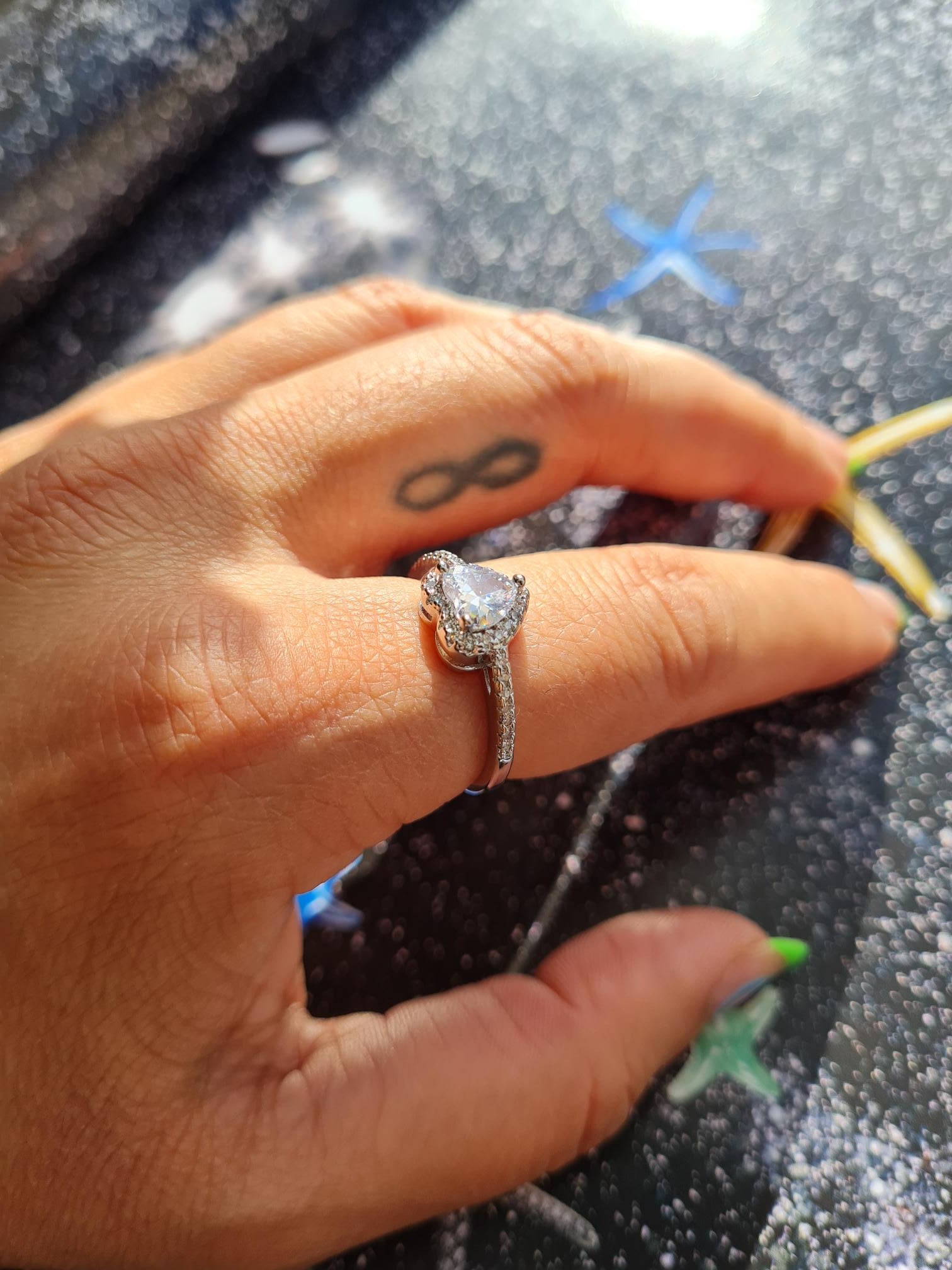 A person's hand displaying an 18k white gold plated sparkle heart ring with a glass cubic zirconia main stone.