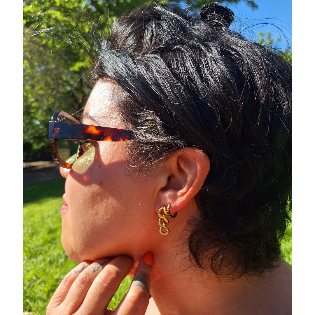 Person wearing stainless steel gold plated curb chain earrings in a park along with turtle shell style sunglasses.