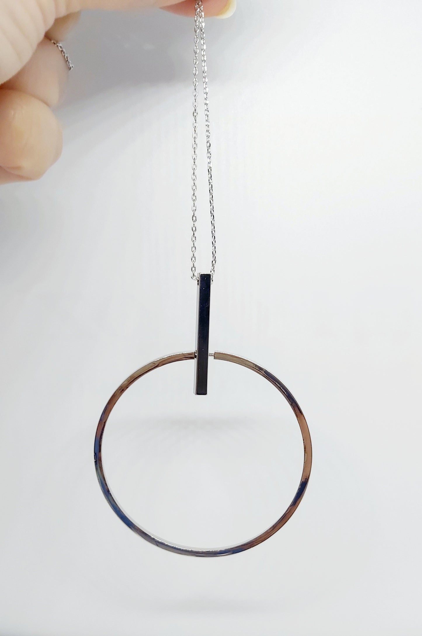 A silver-plated brass necklace with a geometric pendant in the shape of a circle and a bar, displayed on a white background.