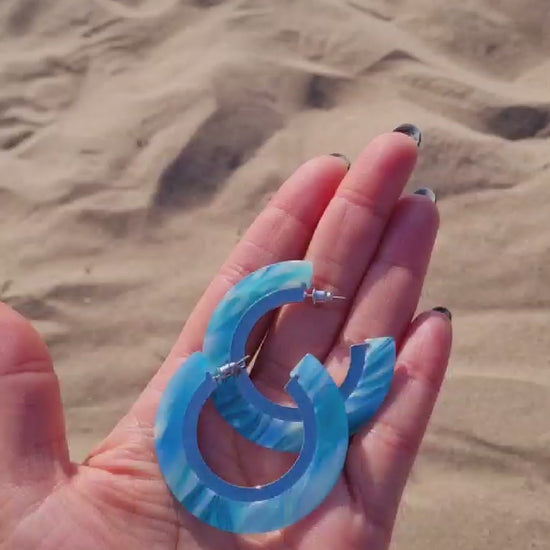 Recycled Under the Sea Resin Hoops in a hand held up on a sandy beach.