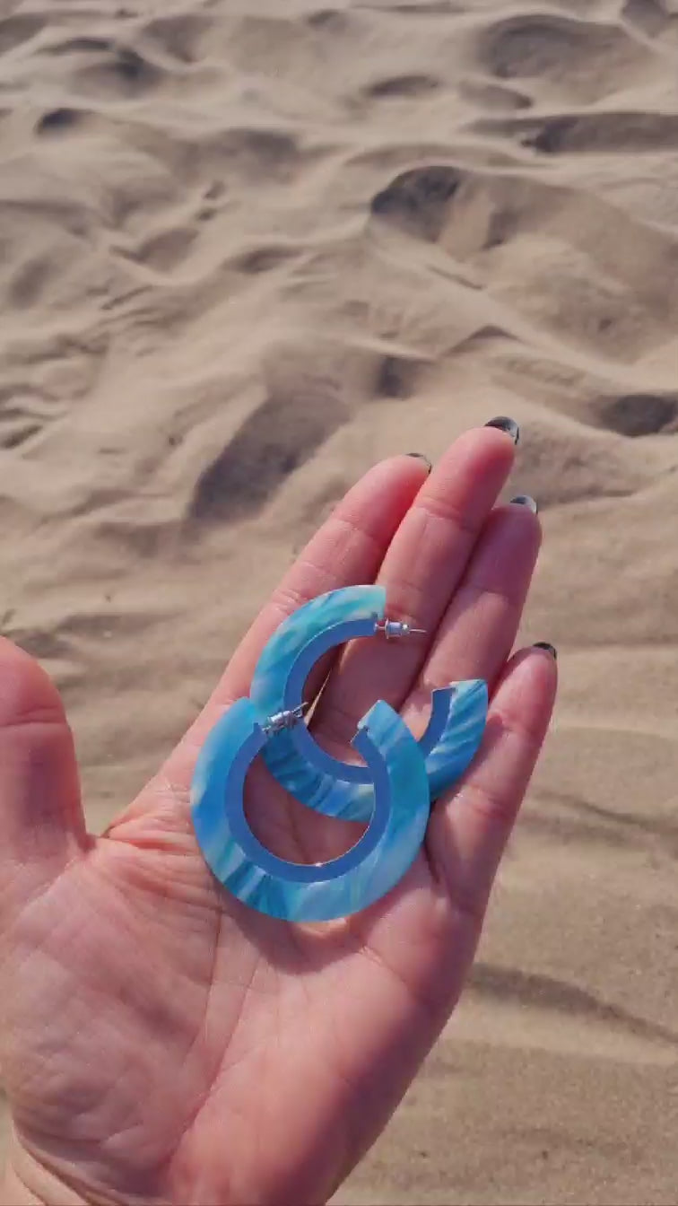 Recycled Under the Sea Resin Hoops in a hand held up on a sandy beach.