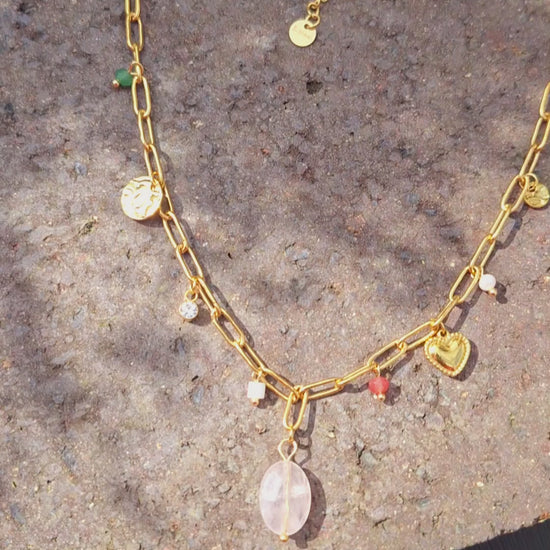 A 18K Gold Plated Rose Quartz Charm Necklace in the sun on a stone Slab.