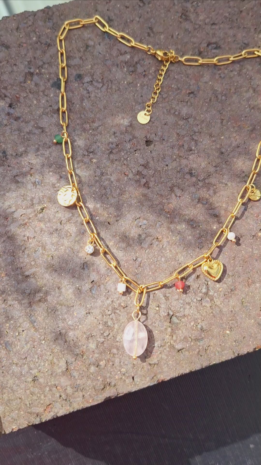 A 18K Gold Plated Rose Quartz Charm Necklace in the sun on a stone Slab.
