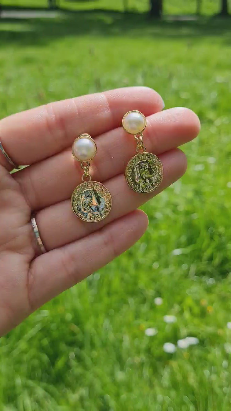 Decadent 14K Gold Plated Coin and Pearl Earrings being held up in the park in the sun.