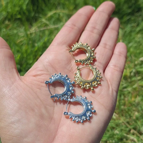 A hand laid flat folding 2 pairs of Arabian creole hoops in the sun. In gold and silver plaiting. 