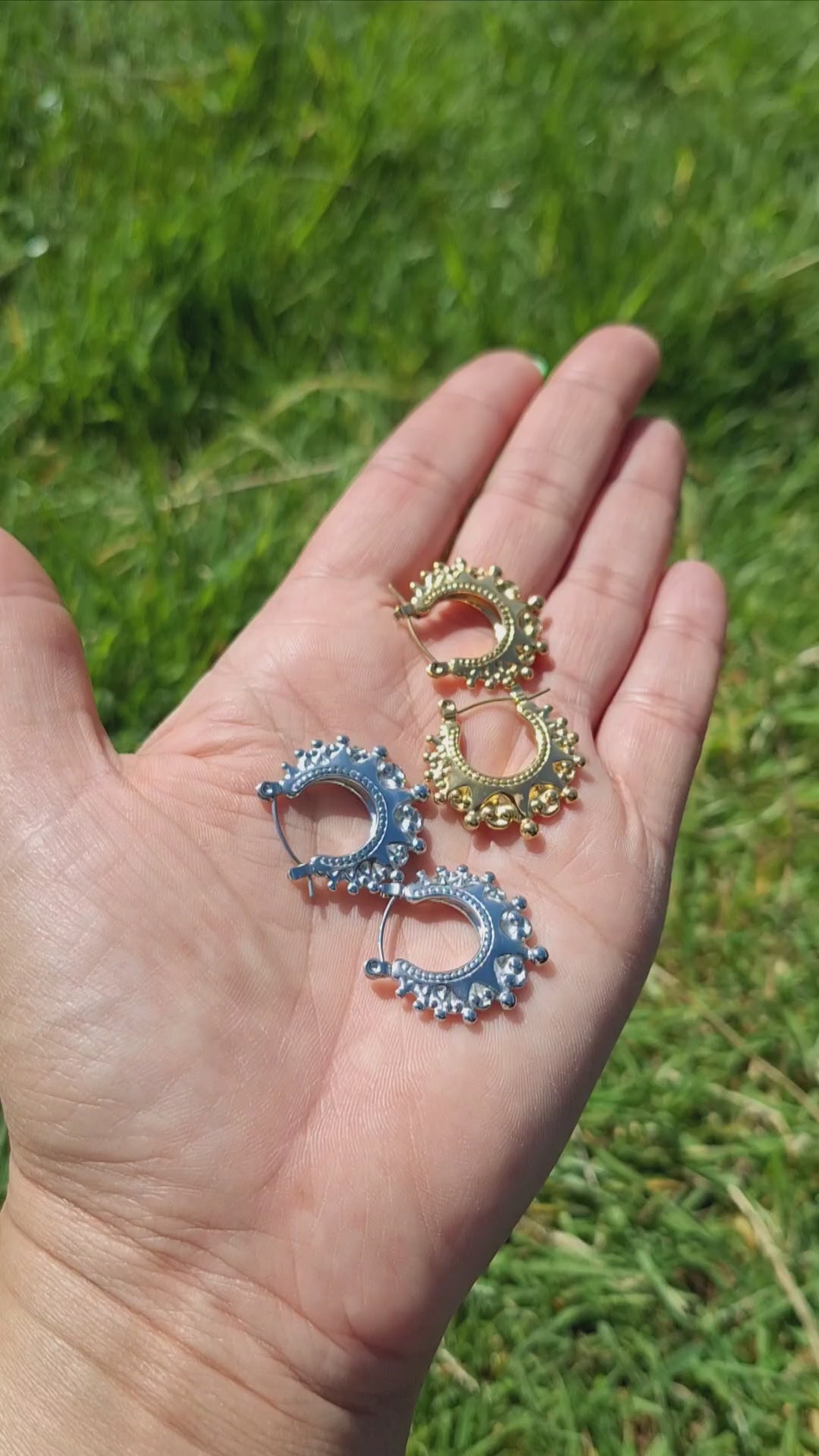 A hand laid flat folding 2 pairs of Arabian creole hoops in the sun. In gold and silver plaiting. 