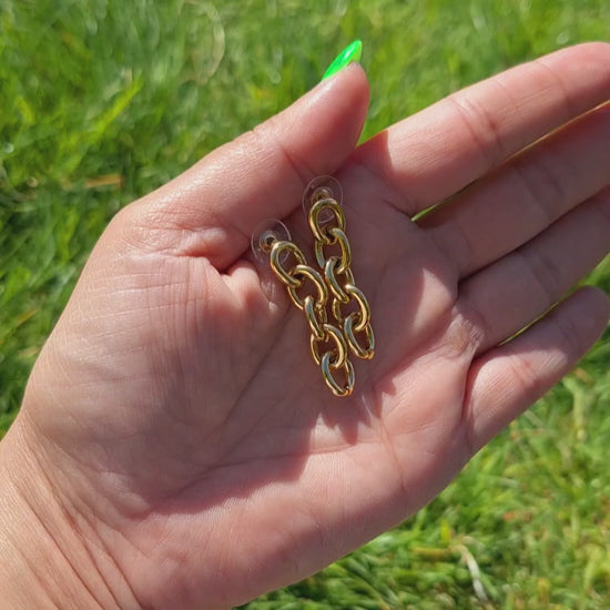 Gold Biker Chain Drop Earrings being held in  hand in the park.