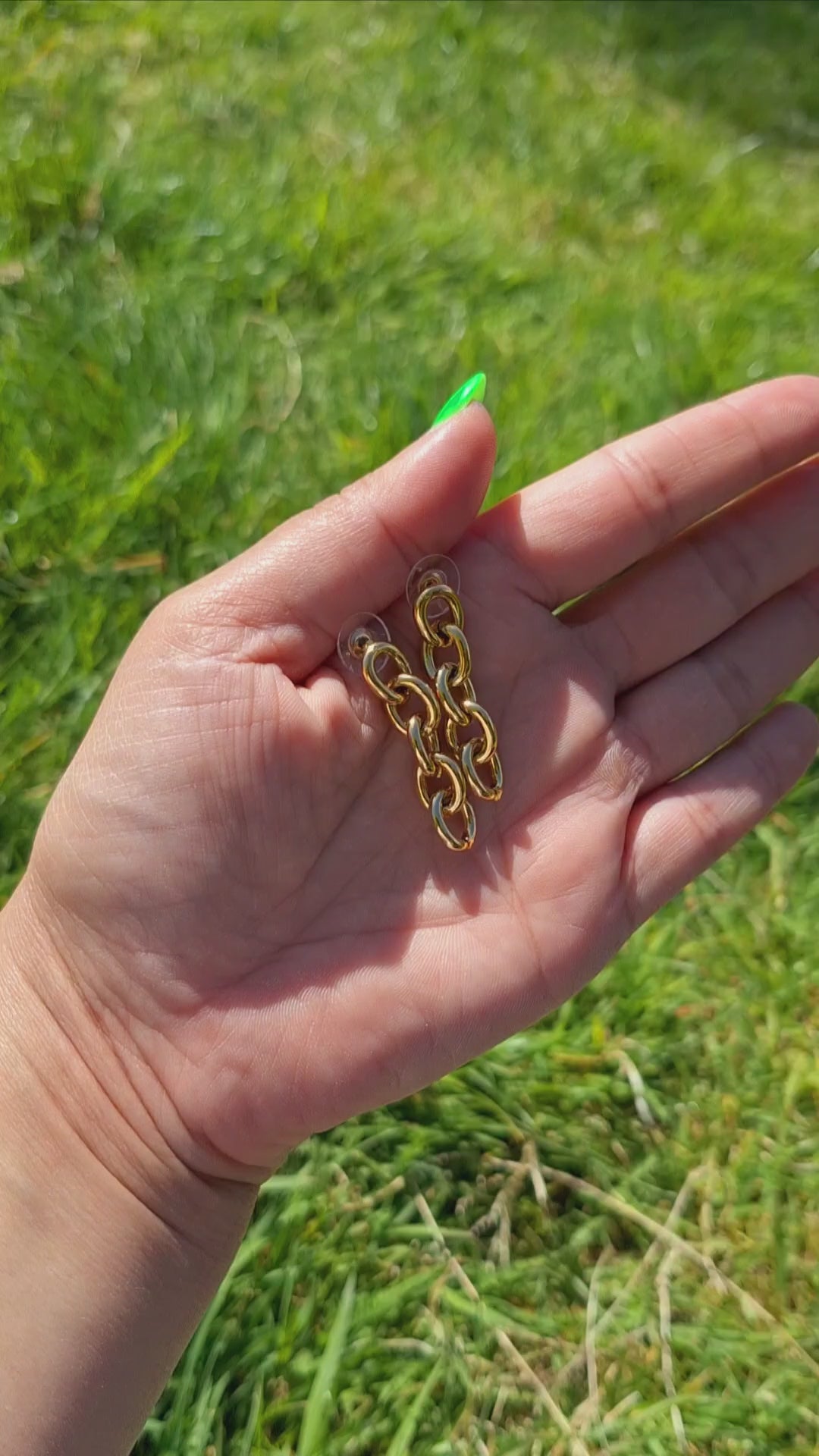 Gold Biker Chain Drop Earrings being held in  hand in the park.