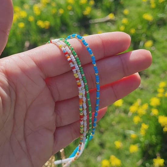 A mixture of handmade beaded necklaces with a gold plated chain s and a crystal miyuki beads being held up with a hand in the park.