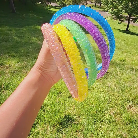 Bright rhinestone summer headbands in various colours being held by a hand in a park in the sun.