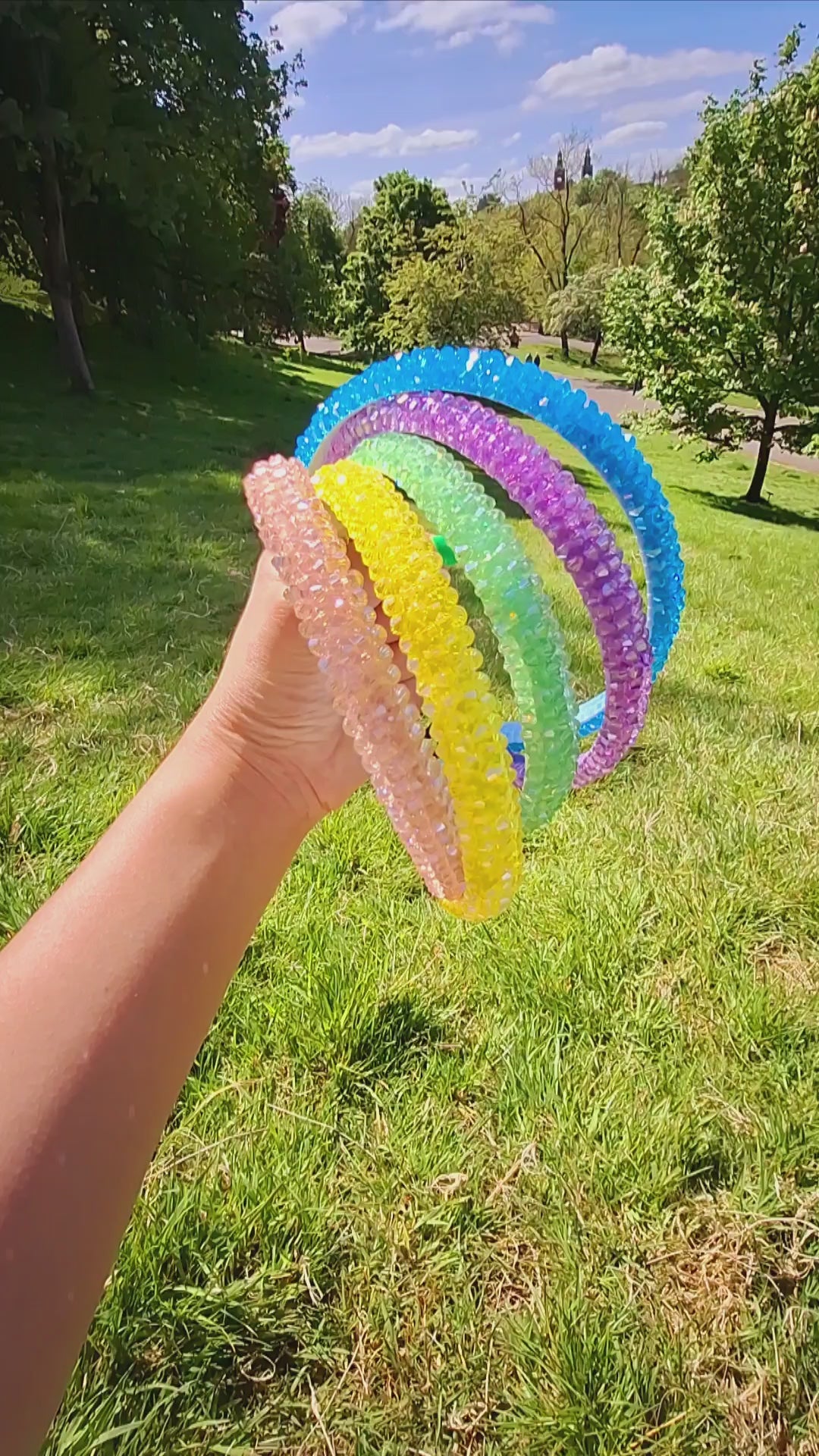 Bright rhinestone summer headbands in various colours being held by a hand in a park in the sun.