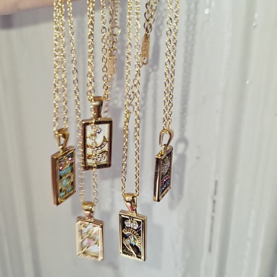 18K gold plated tarot card necklaces with a pendant being held up in the sun.