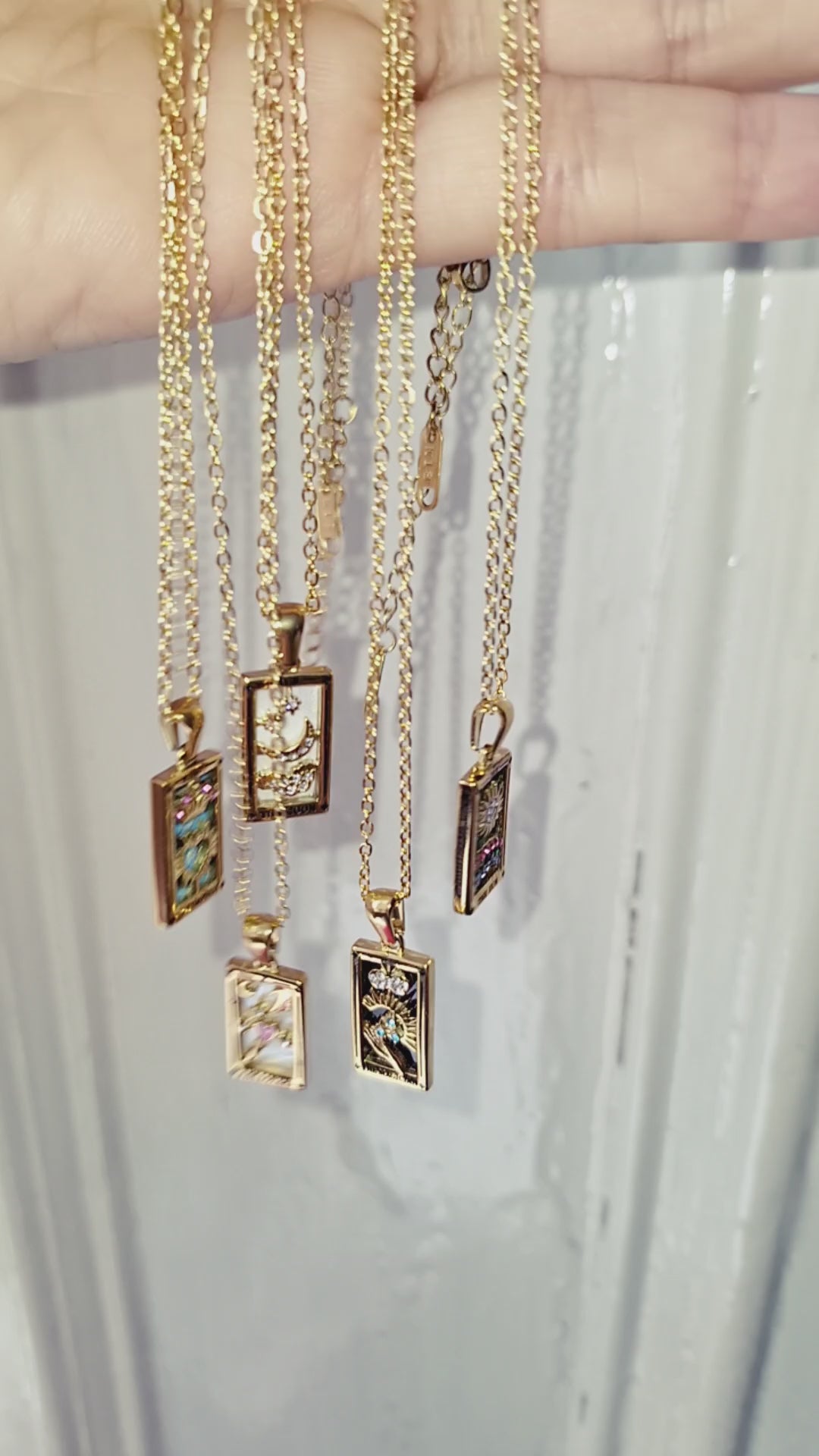 18K gold plated tarot card necklaces with a pendant being held up in the sun.