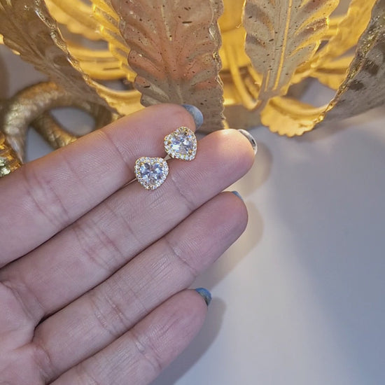14k Gold Plated Sweetheart Stud Earrings held in a hand in the light of a lamp sparking.