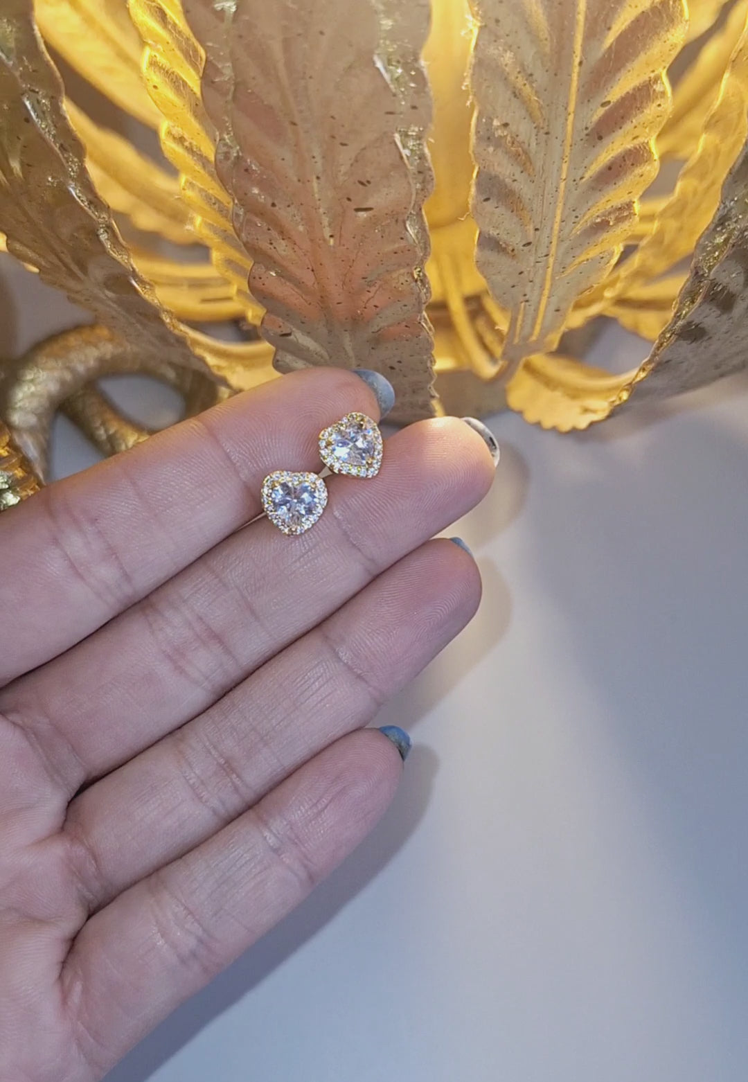 14k Gold Plated Sweetheart Stud Earrings held in a hand in the light of a lamp sparking.