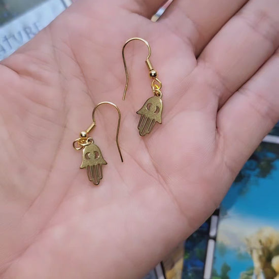 Gold Plated Fatima Hand Earrings featuring the shape of the Fatima hand symbol, displayed on a wooden surface.
