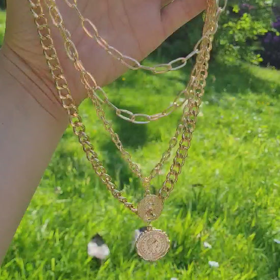 A gold-plated ,multi layer chunky coin necklace displayed on a hand in the sun.