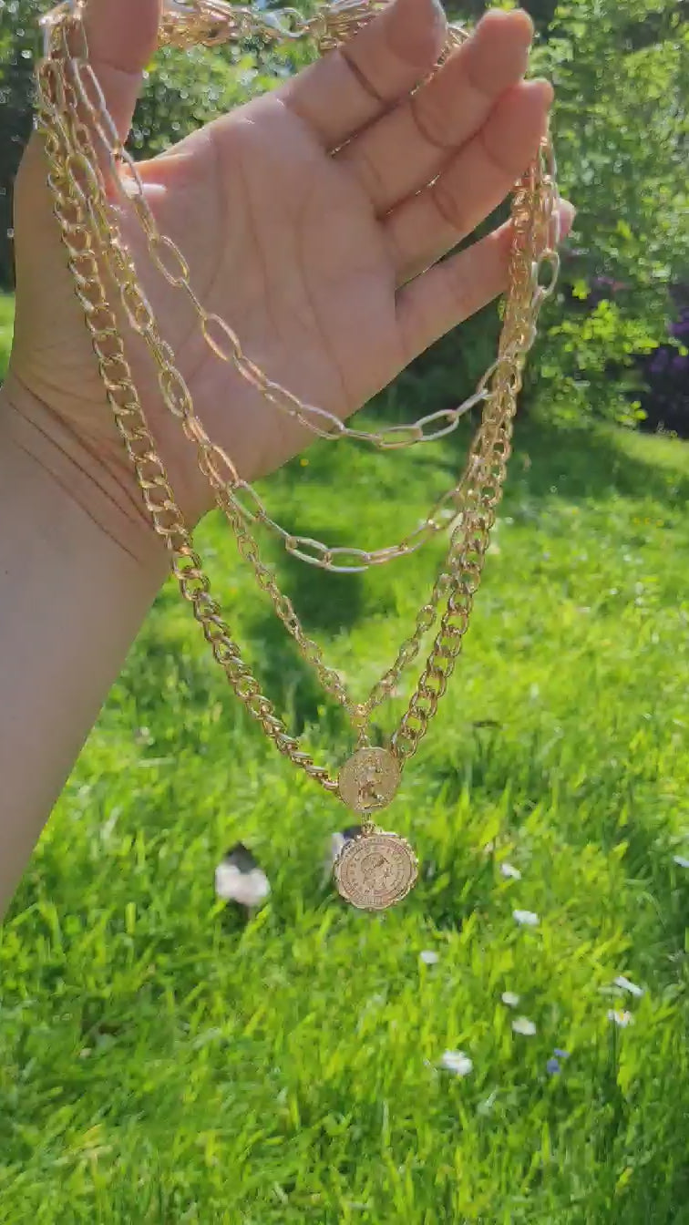 A gold-plated ,multi layer chunky coin necklace displayed on a hand in the sun.